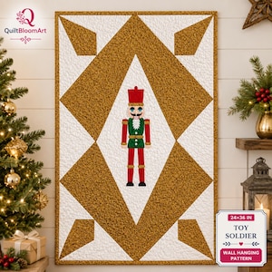 May include: A rectangular wall hanging quilt pattern featuring a central nutcracker figure in red, green, and gold. The design includes a large gold diamond shape on a white textured background. Text on the label reads 24x36 IN TOY SOLDIER.