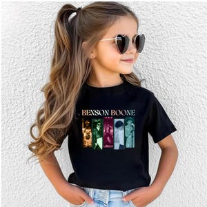 May include: A black short-sleeved t-shirt featuring the text BENSON BOONE in a gradient font above five vertical rectangular panels displaying various photographic images of a performer in different poses and lighting settings.