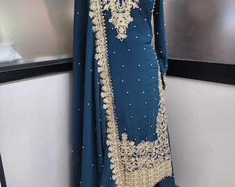May include: A teal long-sleeved tunic and skirt set featuring intricate gold embroidery around the neckline and hem. The garment is embellished with scattered white pearls throughout the fabric and includes a matching teal shawl draped over one shoulder.