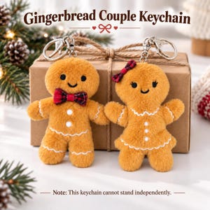 May include: Two plush gingerbread person keychains with metal lobster clasps. One features a red and black plaid bowtie, the other a matching plaid hair bow. Both have embroidered black eyes, smiles, and white icing-style trim on their bodies.