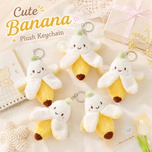 Puede incluir: Cinco llaveros de peluche con forma de plátano, con cáscaras blancas y centro amarillo, cada uno con una cara sonriente de mejillas rosadas y una anilla metálica. El texto "Cute Banana Plush Keychain" aparece en la esquina superior izquierda.