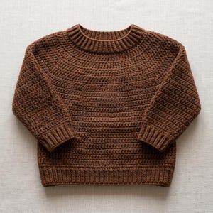 May include: A solid brown long-sleeve sweater featuring a thick ribbed crew neckline, ribbed cuffs, and a ribbed hem. The garment is constructed with a consistent crochet stitch pattern throughout the body and sleeves, creating a textured appearance.