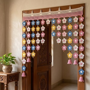 May include: A crochet door curtain featuring a top valance with a grid pattern in cream and pink. Hanging from the valance are multiple vertical strands of crocheted flowers in blue, yellow, white, and pink, interspersed with small brown wooden beads.