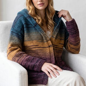 May include: A long-sleeve hooded cardigan featuring a gradient color pattern that transitions from deep teal at the shoulders to a warm golden yellow in the middle and a rich plum purple at the hem and cuffs, crafted with a chunky knit texture.