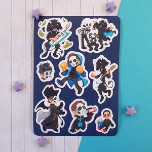 May include: A sticker sheet featuring eight distinct cartoon-style illustrations of characters with pale faces and dark features. The designs include figures playing a keytar and guitar, wearing boxing gloves, a top hat, or drinking from a can.