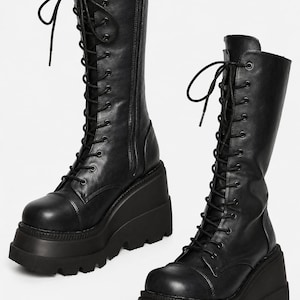 May include: A pair of black knee-high boots featuring a lace-up front with black eyelets and laces, a side zipper closure, and a thick, chunky wedge platform sole with a deep-treaded lug pattern for added height and stability.