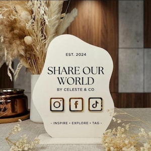 May include: An irregular, off-white social media display sign featuring the text EST. 2024, SHARE OUR WORLD, BY CELESTE & CO, and INSPIRE • EXPLORE • TAG. It includes three gold-bordered square icons for Instagram, Facebook, and TikTok.