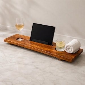 May include: A rectangular wooden bath tray with a dark brown finish featuring a central slot for a tablet, a circular cutout for a stemmed wine glass, and a flat surface area holding a glass of water and a rolled white cotton hand towel.