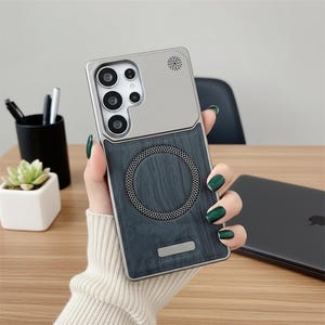 May include: A rectangular smartphone case featuring a metallic silver upper section with a camera cutout and a dark gray wood-grain textured lower section. A circular magnetic charging ring is centered on the back, with a small silver rectangular accent.