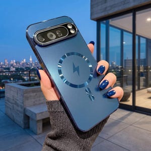 May include: A dark blue smartphone case with a matte finish, featuring a circular magnetic charging ring with a central lightning bolt icon. The case includes a raised rectangular camera module cutout at the top and a small metallic accent below.