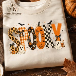 May include: A cream-coloured sweatshirt featuring the word SPOOKY in large, decorative letters. Each letter has a unique pattern including leopard print, orange plaid, floral, jack-o'-lanterns, and black-and-white checkers, with small ghosts and bats.