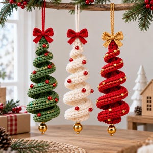 May include: Three spiral-shaped crochet Christmas tree ornaments hanging from a branch. The trees are green, white, and red, each topped with a crocheted bow and decorated with small beads. A shiny gold sphere hangs from the bottom of each tree.
