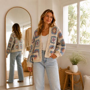 May include: A long-sleeve open-front cardigan made of cream-colored yarn with a multi-colored granny square pattern in shades of blue, pink, and purple. The garment features two front pockets, each adorned with three small crocheted flower appliqués.