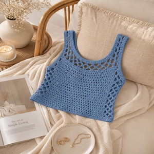 Peut inclure: Un débardeur bleu en crochet sans manches présentant un motif ajouré en forme de losange le long de l'encolure et sur les côtés, avec un corps en mailles carrées pleines. Le vêtement est en fil bleu avec une encolure dégagée et des bretelles.