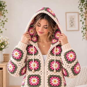 Pode incluir: Um casaco com capuz e fecho de correr feito de quadrados de crochet com um padrão floral em creme, verde escuro e rosa brilhante. A peça inclui um capuz com cordões compridos em tom creme rematados com contas de madeira e punhos canelados.