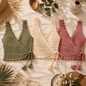 Peut inclure: Trois hauts sans manches style cache-cœur en vert olive, crème et vieux rose. Chaque haut présente un motif en maille crochetée ouverte, une encolure en V, des bords festonnés le long de la garniture et une fermeture à nouer sur le côté.