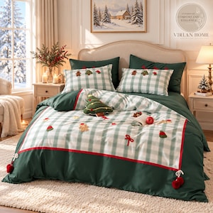 Pode incluir: Um conjunto de roupa de cama com padrão xadrez branco e verde claro com motivos natalícios bordados, incluindo figuras de pão de mel, árvores e laços vermelhos. A capa de edredão tem uma borda verde escura com debrum e pompons vermelhos.