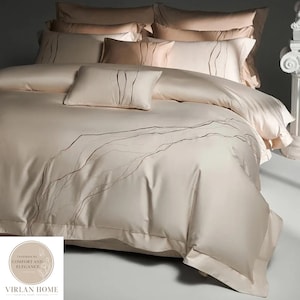 May include: A beige bedding set featuring a duvet cover and multiple pillows with a smooth, satin-like finish. The duvet and pillows are decorated with delicate, dark brown embroidered wavy lines. The brand logo Virlan Home is visible.