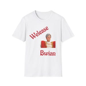 Può includere: Una t-shirt bianca a maniche corte con la grafica di un uomo in toga rossa con i capelli grigi. Il testo "Welease" è stampato in rosso sopra la grafica, mentre il testo "Bwian" è stampato in rosso sotto la grafica sul davanti della maglia.