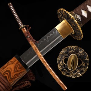 Könnte beinhalten: Ein japanisches Katana-Schwert mit einer scharfen Stahlklinge mit sichtbarer wellenförmiger Härtelinie, einem braun umwickelten Griff und einer Messingzwinge. Die Scheide hat eine Holzmaserung mit braunen Kordelakzenten und einen runden Messingstichblatt.