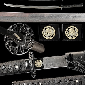 May include: A katana sword featuring a folded steel blade with a visible grain pattern, a black wrapped handle, and a circular chain-link guard. The sword includes a black scabbard with a cord wrap and a gold-toned circular emblem on the collar.
