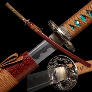 Może przedstawiać: Miecz katana ze srebrnym ostrzem z falistą linią hamon, rękojeścią owiniętą sznurkiem w kolorze opalenizny z turkusową wstawką ze skóry płaszczki oraz okrągłym metalowym jelcem z motywami smoków. Pochwa posiada czerwono-czarny wzór spękań.