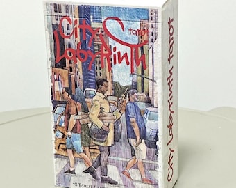 May include: A rectangular deck of City Labyrinth tarot cards featuring a colourful illustration of people walking on a city street. The box displays the title in red text, includes 78 tarot cards and a guidebook, and shows urban buildings.