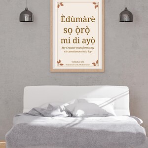 May include: A framed wall art print featuring the Yoruba text Èdùmàrè sọ ọ̀rọ̀ mi di ayọ̀, with the English translation My Creator transforms my circumstances into joy, accented by small brown leaf illustrations in the corners.