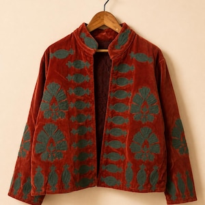 Könnte beinhalten: Eine rostfarbene Samtjacke mit Stehkragen und langen Ärmeln. Das Kleidungsstück ist mit dunkelgrünen, gestickten Blumen- und geometrischen Mustern auf der Vorderseite und den Ärmeln verziert. Der Text HEVENCRAFTINDIA ist sichtbar.