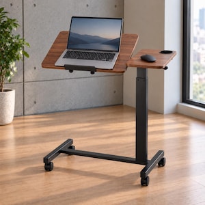 Puede incluir: Un escritorio móvil para portátil con acabado de veta de madera oscura, que cuenta con una superficie inclinable ajustable para el ordenador y una plataforma lateral fija más pequeña con un portavasos integrado. Estructura de metal negro y cuatro ruedas.
