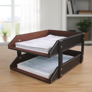 Pode incluir: Uma bandeja de documentos de dois níveis com exterior castanho escuro com costuras brancas contrastantes e interior castanho claro. A bandeja contém pilhas de documentos de papel branco em ambos os níveis, fixadas por suportes laterais.