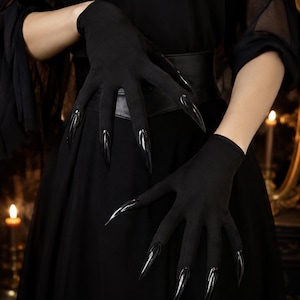 May include: A pair of black gloves featuring long, pointed, glossy black claw-like extensions attached to each fingertip. The gloves are made of a smooth, opaque fabric that covers the hands and wrists, creating a sharp, elongated silhouette.