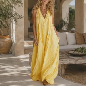 May include: A floor-length, sleeveless yellow dress with a deep V-neckline and a loose, flowing silhouette. The garment features a simple, unpatterned design with a soft, draped fabric that falls to the floor, creating a relaxed and comfortable look.