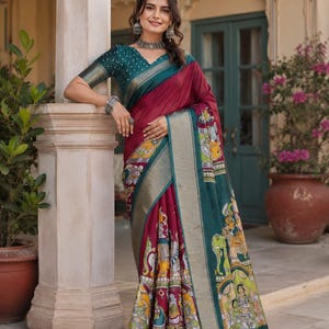 May include: A maroon saree featuring a teal blouse with white polka dots and a wide teal border. The saree displays intricate multi-colored figurative illustrations along the hem and pallu, complemented by a metallic silver-toned border finish.
