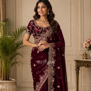 Può includere: Un sari color bordeaux intenso caratterizzato da intricati ricami dorati lungo i bordi e motivi floreali sparsi su tutto il tessuto. La blusa abbinata presenta maniche corte e uno scollo rotondo, con il testo MSTFAB6 visibile sul capo.