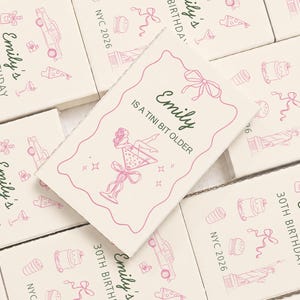 May include: Rectangular white cards featuring pink line art illustrations of a martini glass with a person inside, a bow, and the text 'Emily IS A TINI BIT OLDER'. Other cards show 'Emily's 30TH BIRTHDAY' with icons of a cake, car, and Statue of Liberty.