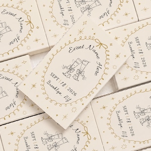 May include: A collection of rectangular off-white cards featuring a gold foil-stamped oval border with stars. Each card displays a black ink illustration of two champagne flutes with bows, the text Event Name Here, and SEPT 18 2026 Brooklyn, NY.