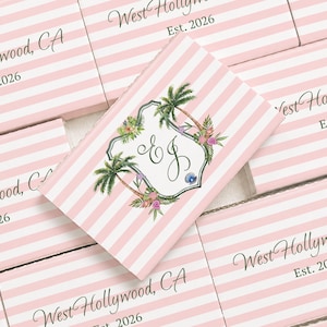 May include: A rectangular card featuring a light pink and white striped pattern. The text West Hollywood, CA Est. 2026 is printed in black. A central white label displays the cursive monogram EJ surrounded by palm trees and colorful flowers.