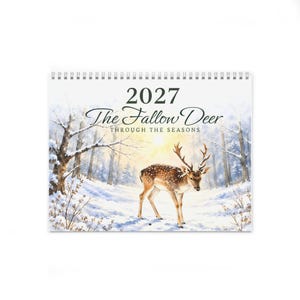 Op de afbeelding: Een wandkalender voor 2027 met de titel The Fallow Deer Through The Seasons, voorzien van een aquarelillustratie van een gevlekt damhert in een besneeuwd boslandschap met kale bomen en een zacht gouden licht op de achtergrond.