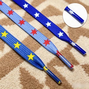 May include: Three flat shoelaces featuring star patterns. One lace is dark blue with white stars, one is light blue with red stars, and one is medium blue with yellow stars. Each lace has a clear plastic aglet at the end for easy threading.