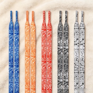May include: Five pairs of flat shoelaces arranged vertically, each featuring a distinct paisley pattern. The colors include blue, orange, red, black, and white, with each pair displaying a matching design and aglets at the top ends.