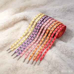 May include: A collection of flat shoelaces featuring various fruit and food patterns, including yellow bananas, purple grapes, pink watermelons, orange peaches, and red strawberries. Each lace has a silver metal aglet at the end for easy threading.