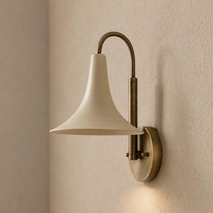 Peut inclure: Une applique murale composée d'un abat-jour en forme de trompette blanc cassé mat fixé à un bras métallique incurvé au fini laiton antique. Le luminaire comprend une plaque murale circulaire en laiton et un support cylindrique vertical.