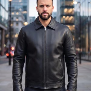 May include: A black leather jacket featuring a classic point collar, long sleeves with buttoned cuffs, and a full-length silver-toned metal zipper closure down the center. The jacket includes two vertical side pockets and a smooth, clean finish.