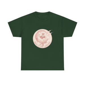 Peut inclure: Un t-shirt vert foncé avec un motif circulaire au centre. Le design présente un croissant de lune, un télescope et une grappe de cerises avec un nœud, le tout dans des tons rose clair. Le texte "Made Of Star Leftovers" est imprimé.