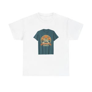 Könnte beinhalten: Ein weißes Kurzarm-T-Shirt mit einer mittigen Grafik eines blaugrünen T-Shirts. Die Grafik zeigt einen Hirschkopf mit Geweih, gekreuzte Gewehre und einen Sonnenuntergangshintergrund mit dem Text "COUNTING DOWN TO OPENING DAY" auf einem Banner.