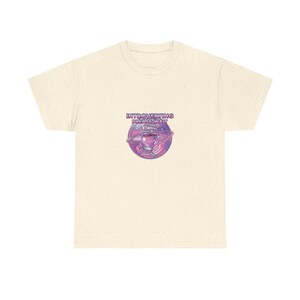 May include: A cream-colored short-sleeve t-shirt featuring a circular graphic on the chest. The design depicts a steaming cup of coffee inside a purple and pink galaxy, surrounded by the text "INTROVERTING PLEASE WAIT" in a bold, rounded font.