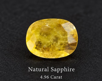 May include: A faceted oval-shaped yellow natural sapphire gemstone with visible internal inclusions. The text below the stone reads Natural Sapphire 4.96 Carat. The gemstone displays a bright golden-yellow hue with multiple geometric facets.