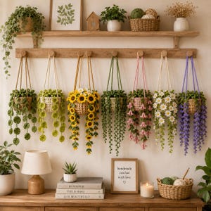 Puede incluir: Siete cestas colgantes de ganchillo en varios colores y diseños florales, incluyendo girasoles, margaritas y enredaderas, suspendidas de un estante de pared de madera sobre una mesa con libros, una lámpara y un letrero que dice handmade crochet with love.
