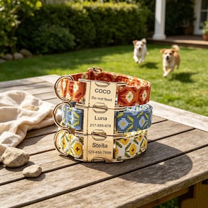 May include: Three stacked dog collars featuring geometric patterns in orange, blue, and yellow. Each collar has a gold-tone metal buckle engraved with names and contact information: Coco with Do not feed, Luna with 217-555-678, and Stella with 123-456-7890.